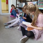 Uczennice czytaja książki przy półkach w bibliotece..jpg