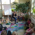 Uczennica czyta książkę dzieicom_ które siedzą na kolorowym dywanie..jpg