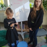 Dziewczynka stoi przy tablicy i  rozwiązuje zagadkę na kartce.jpg