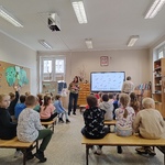 Uczniowie siedzą na łąwkach i słuchają nauczyciela.jpg