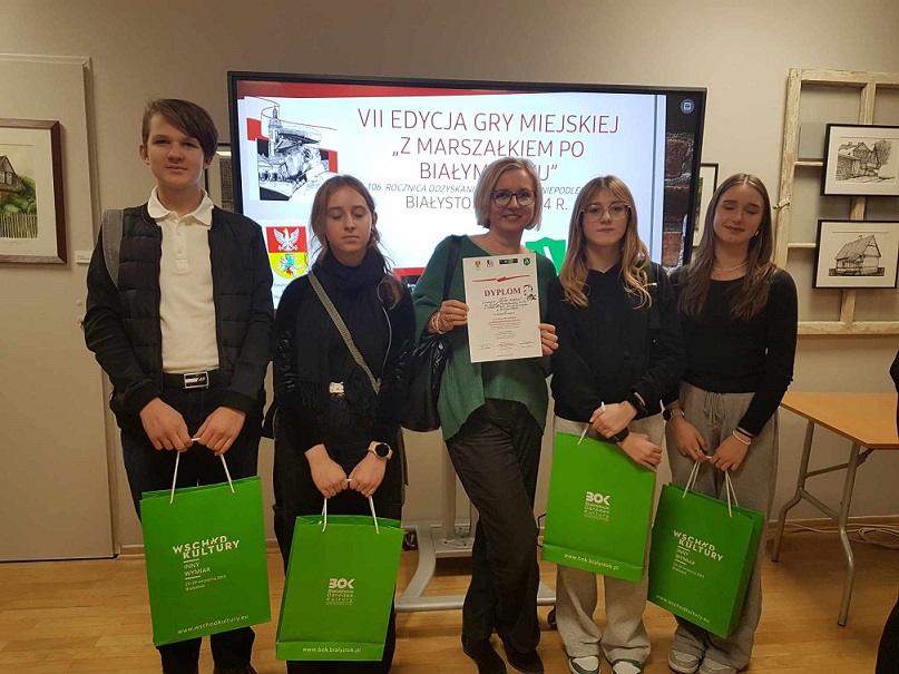 Uczniowie razem z nauczycielką pozują do zdjęcia_ trzymają w rękach zielone torby.jpg