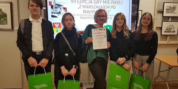 Uczniowie razem z nauczycielką pozują do zdjęcia_ trzymają w rękach zielone torby.jpg