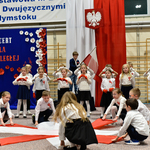 Grupa dzieci tańczy z biało-czerwonymi szarfami.