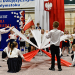 Grupa dzieci tańczy z biało-czerwonymi szarfami.