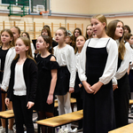 Grupa dziewczynek ubrana na galowo śpiewa pieśni.