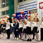 Grupa dzieci ubrana na galowo macha w górze flagami biało-czerwonymi.