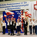 Grupa dzieci ubrana na galowo macha w górze flagami biało-czerwonymi.