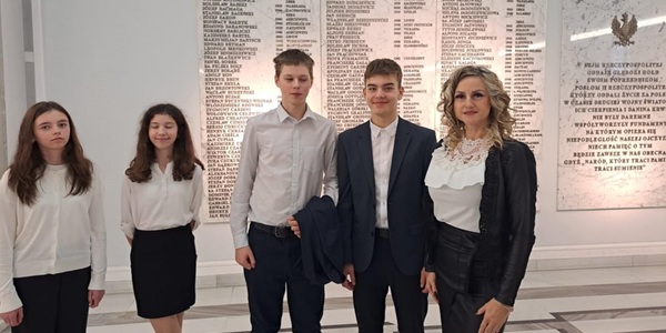 Uczniowie i nauczycielka ubrani na galowo stoją przy tablicy z napisami.jpg