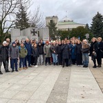 Duża grupa uczniów i opiekunów stoi na podwórku przed budynkiem parlamentu.jpg