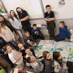 Grupa uczniów siedzi i stoi wokół plakatu.jpg