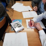 Stół z listami i osobami piszącymi na nich.jpg