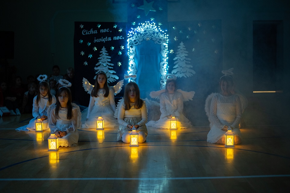 Dziewczynki przebrane za aniołków siedzą z lampionami.