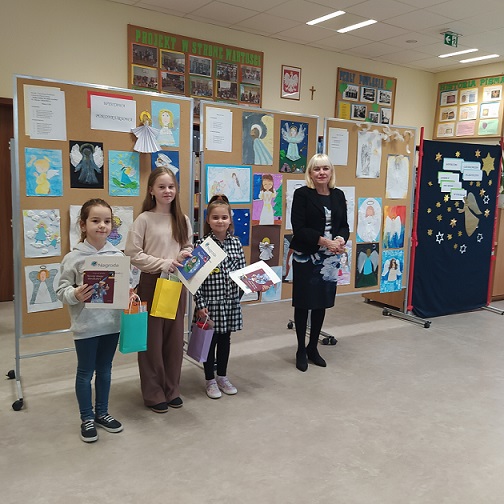 Trzy dziewczynki stoją obok nauczycielki przy kolorowych tablicach z rysunkami..jpg