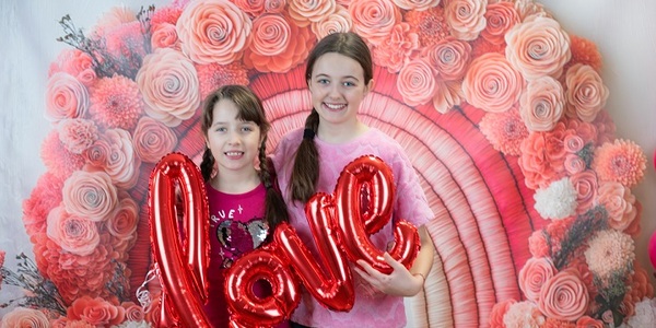 Dwie dziewczynki trzymają napis love na tle różowych kwiatów