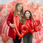 Pani z dziewczynką trzymają napis love na tle różowych kwiatów