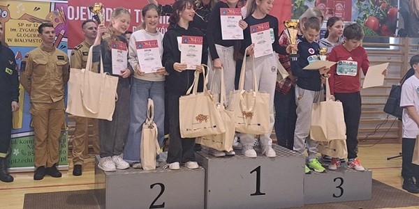 Grupa dziewczyn stoi na podium z dyplomami i upominkami.jpg
