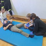 Uczennice opatruja ranę nogi u mężczyzny.jpg
