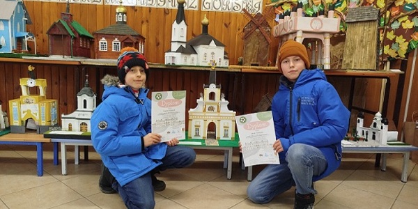Dwóch chłopców pozuje z dyplomami na tle makiet z zabytkami.jpg